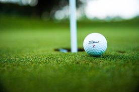 Golfball am grünen Rasen neben Einschlagloch