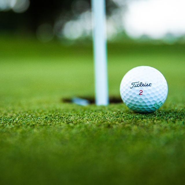 Golfball am grünen Rasen neben Einschlagloch